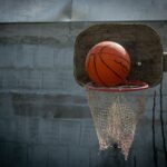 Close-up of a basketball on an outdoor hoop with a worn net and wooden backboard.